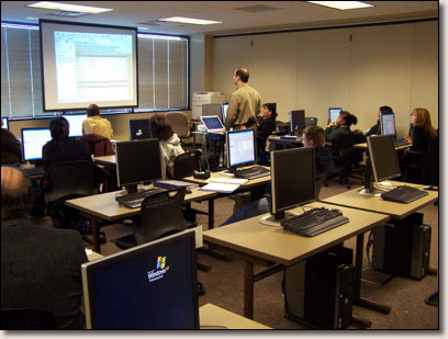Instructor and students in the computer lab.  Shows multiple desks and computers, with instructor using the overhead projection to demonstrate a point.Photo credit:  NIPTC Staff.